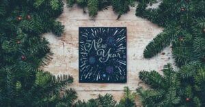 Beautifully written sign signaling the start of the New Year, surrounded by pine boughs.
